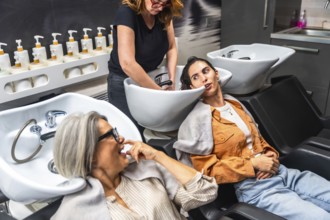 Clients and hairdresser share a laugh while washing hair in a modern salon, enjoying friendly
