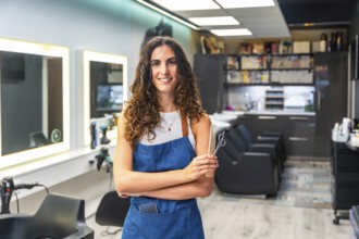 Woman hairstylist entrepreneur smiling, standing in a small business hair salon, holding hair