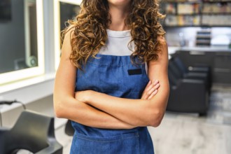 Professional hairdresser with curly hair standing confidently in a hair salon, wearing a stylish