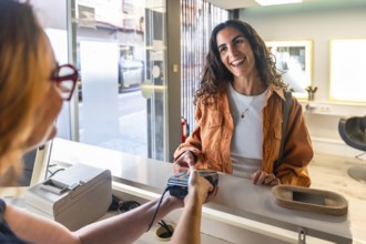 Young woman customer smiles confidently as she makes a secure contactless credit card payment at a