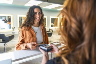 Smiling woman paying with a contactless credit card at a modern hair salon reception, completing a