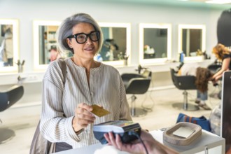 Smiling mature woman paying for hair services by tapping a credit card on a contactless payment