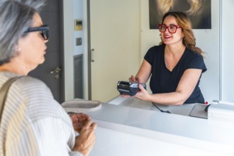 Salon receptionist smiling and processing a contactless credit card payment at the front desk for a