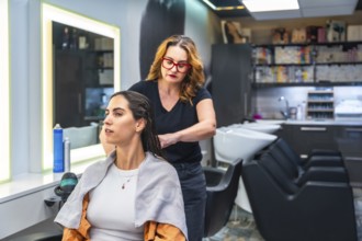 Hairstylist working through a young woman's damp brunette hair in a bright modern salon, preparing