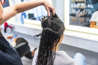 Hairdresser holding sections of wet hair on a woman's head in a bright salon, preparing for a