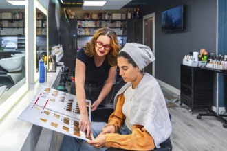 Professional hairstylist advising female client during a beauty consultation, pointing at hair dye