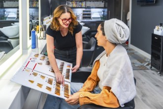 Hairdresser and female client compare a color swatch chart during a friendly consultation in a