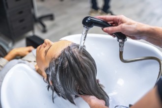 Woman relaxing as hairdresser rinses her hair over a salon sink with a handheld shower, receiving