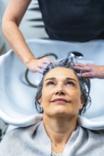 Woman with gray hair receiving a shampoo and head massage from a hairstylist at a modern hair