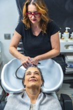 Hair stylist washing a mature woman's hair at the shampoo sink, creating a moment of self care,