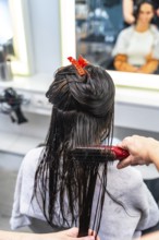 Professional hairdresser gently brushing wet hair of a female client during conditioning and