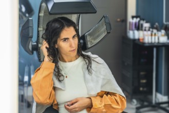 Young woman seated under a professional salon hair dryer, receiving a pampering hair treatment
