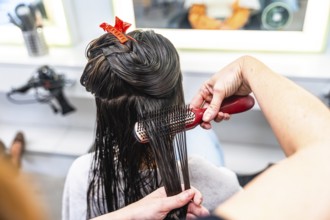 Professional hairdresser brushing through wet, dark long hair with clips, preparing sections for