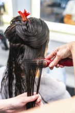 Hairdresser performing a hair styling service on a female client, brushing her wet dark hair after