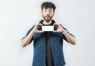 A surprised bearded man showing phone screen isolated. Shocked bearded guy showing promotion on