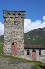 Old stone tower and small building against a mountain backdrop under a deep blue sky, defensive
