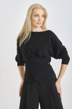 A fashion model stands confidently in a modern black outfit, featuring a stylish wrap design. The