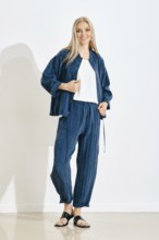 A woman stands in a bright indoor setting wearing a blue outfit made of light fabric. She smiles