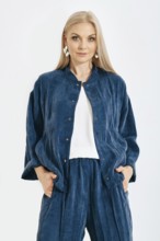 Blonde woman stands with her hands in pockets wearing a denim jacket and matching pants in a studio