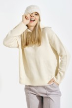 Playful woman pulls his hat over her eye. She is wearing a sweater and a warm pants. She smiles
