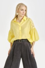 A woman poses confidently in a bright yellow blouse with intricate details, paired with relaxed