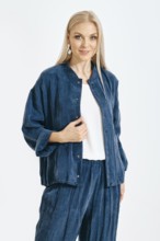 A woman stands in a studio wearing a blue outfit. She poses confidently with a smile. The