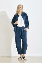 Smiling woman stands in a studio wearing a comfortable outfit, consisting of a matching jacket and