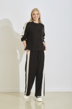 A woman stands confidently in a black and white athletic outfit with pockets, showcasing a modern