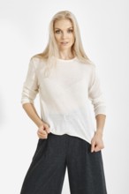 A model stands in a studio wearing a white top and dark wide-leg pants. She showcases the clothing