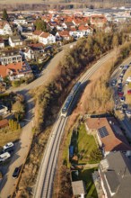 Aerial view of a railway line running through a town with red roofs and surrounding nature, test