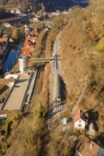 Train travels through a hilly landscape with village and river from a bird's eye view, test trip on