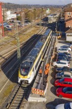 Aerial view of a train station with a passing train and parked cars, test run on the new