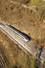 Aerial view of a train traveling through a wooded area surrounded by bare trees, test run on the