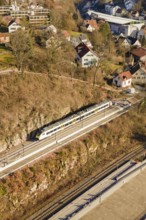 Train travels through a village on elevated tracks surrounded by hills and houses, test run on the