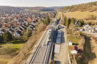 Railway line runs through a village with red-roofed houses, surrounded by trees and meadows, test