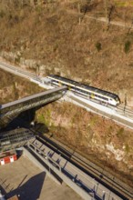 A train crosses a bridge surrounded by bare autumn trees and railroad tracks, test run on the new