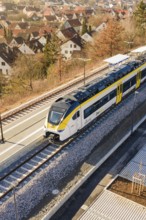 Modern train stands at the station, surrounded by autumn trees and residential buildings, test run