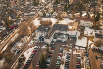 View of a large building complex with parking spaces and surrounding residential area in winter,