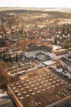 Urban area in winter with snow-covered houses and roads in warm sunlight from a bird's eye view,
