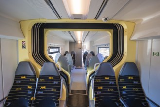 Train compartment with yellow accents and grey seats in bright surroundings, test run on the new