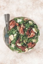Fresh arugula salad with prosciutto and grated parmesan cheese, on a plate, homemade, no people