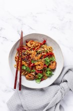 Udon noodles, shrimp with vegetables and fresh herbs, in a bowl with chopsticks, light background,