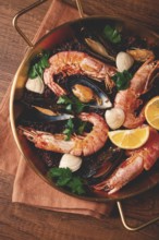 Seafood and black rice paella, in a frying pan, homemade, on a wooden table, no people