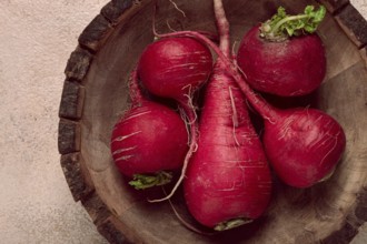 A collection of vibrant red radishes sits in a round wooden bowl, showcasing their natural texture