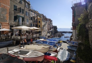 Stacked boats in front of colorful houses under a blue sky in the fishing village of Riomaggiore,