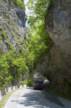 A black van passes a narrow road under a natural rock arch, camper, motorhome in a gorge on the