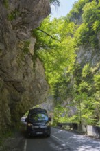 A black van drives along a shady mountain road lined with rocks and trees, camper, motorhome in a