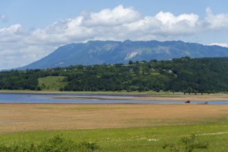 Idyllic landscape with lake, green shore and mountains in the background under a cloudy sky,