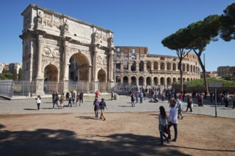 Arch of Constantine and Colosseum surrounded by tourists under blue sky and green grass, Rome,