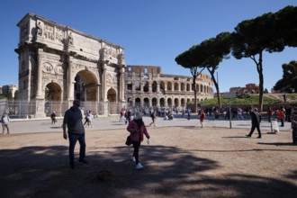 Tourists in front of the Colosseum and Arch of Constantine on a sunny day surrounded by trees,